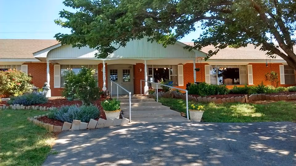 Brick senior living facility entrance with steps, ramp, and landscaped front yard.