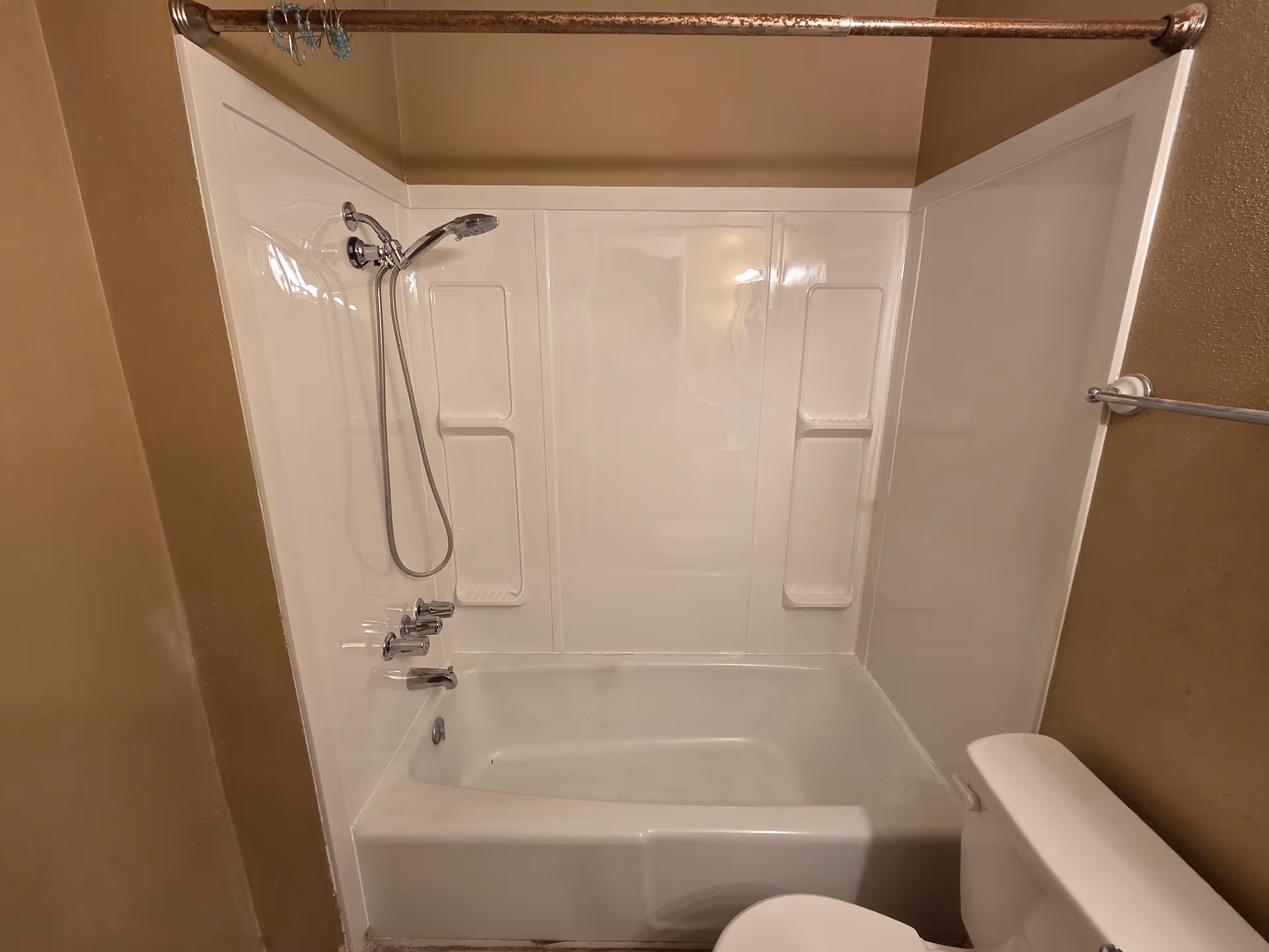 White bathtub with shower surround, chrome fixtures, and towel bar in a small bathroom.