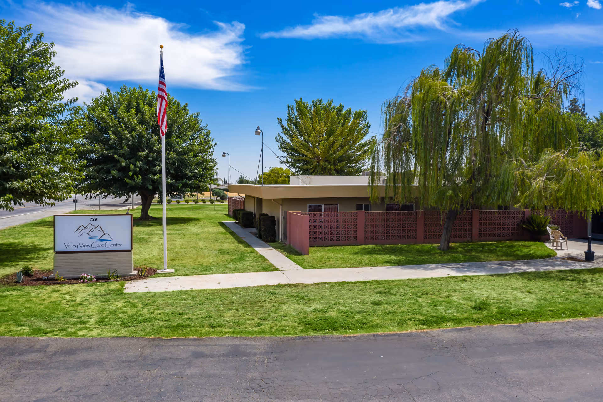 Front exterior of Delano PostAcute Care building with sign, flagpole, and trees.