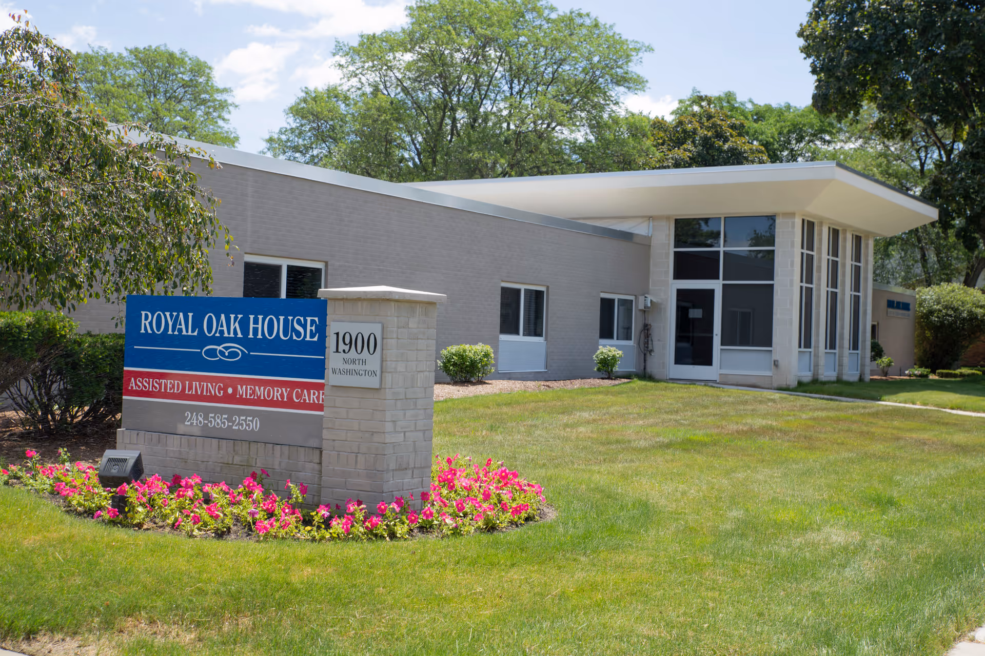 Exterior view of Royal Oak House assisted living facility with sign, plants, and landscaping.