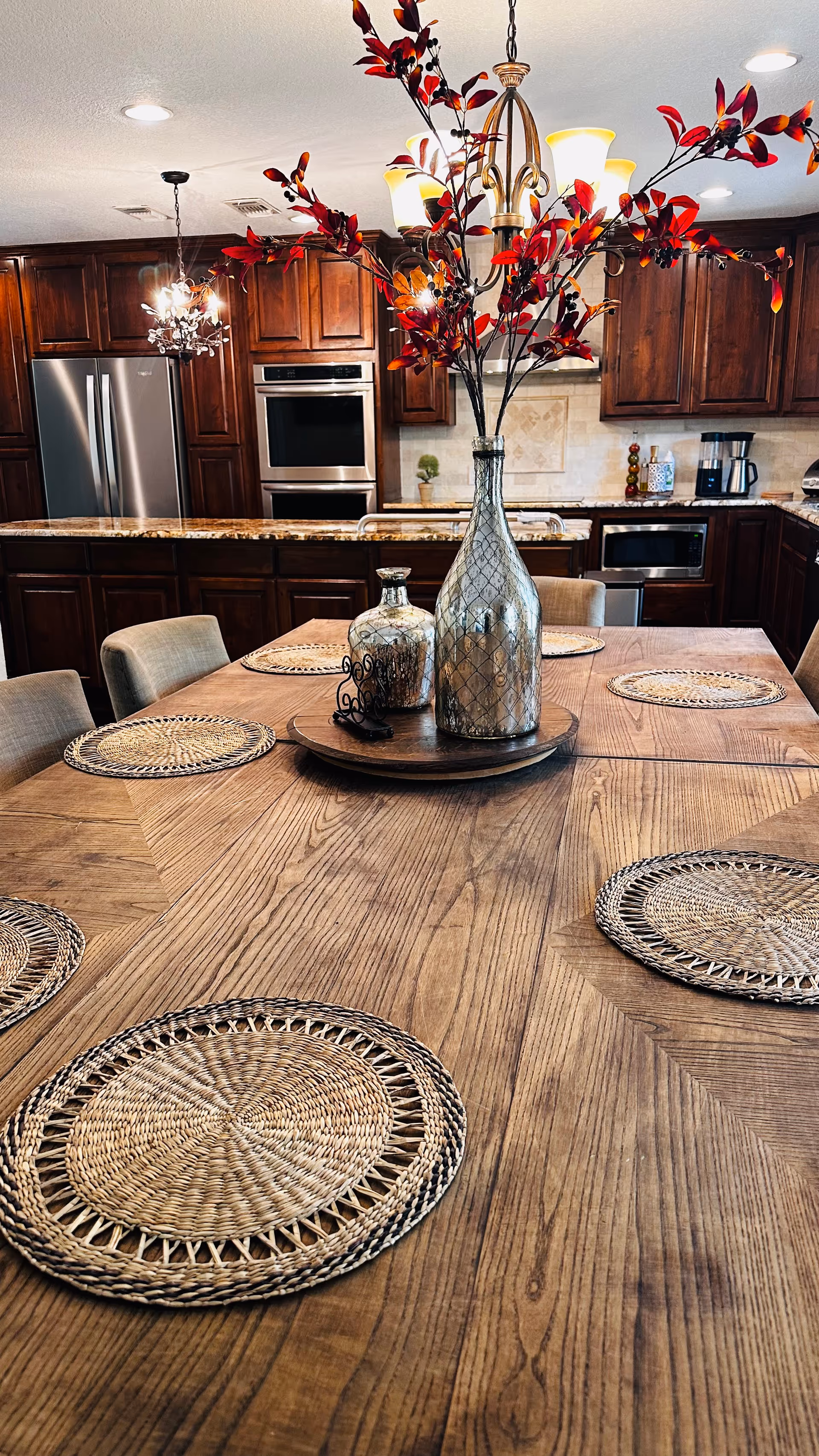 Wooden dining table with woven placemats and vases in a kitchen-dining area.