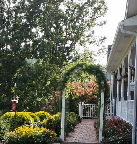 Exterior view of TLC Adult Home showing a brick walkway through a garden arch