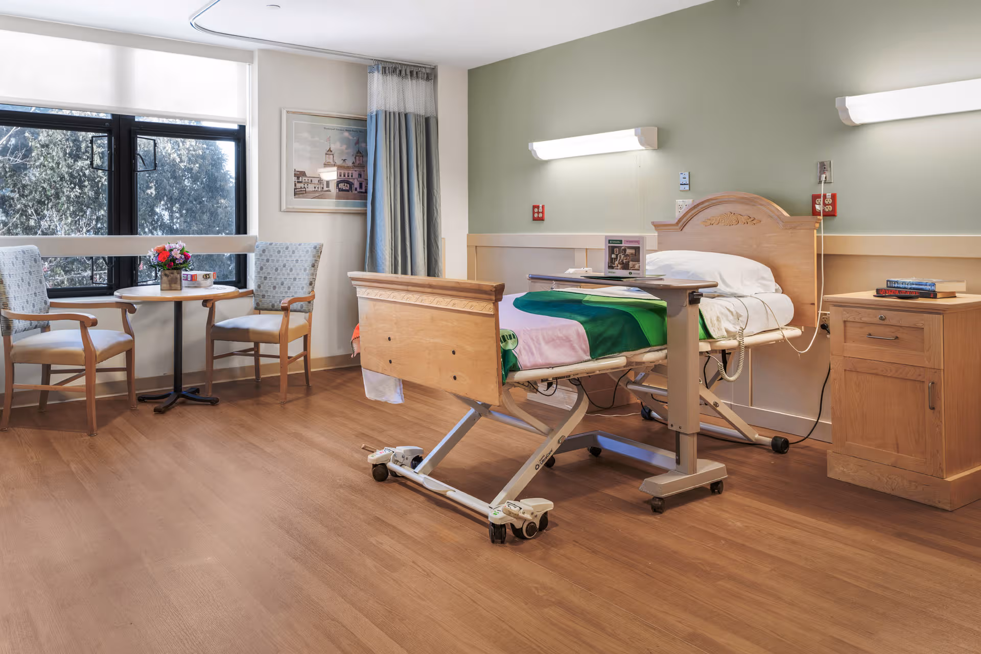 Hospital-style patient room with an adjustable bed, seating area, and a window.