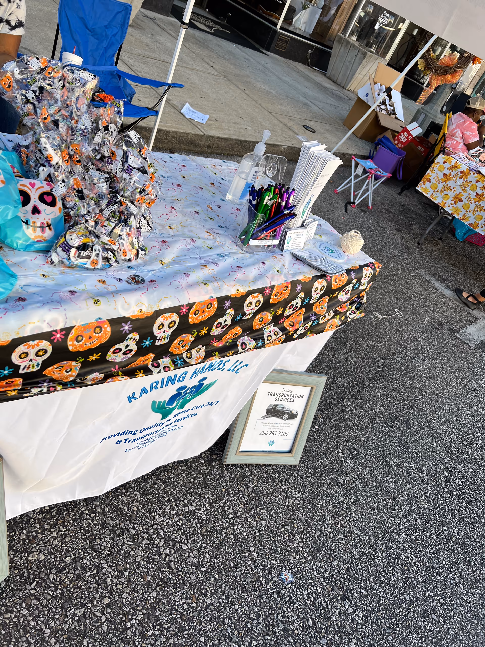 Outdoor vendor table for Karing Hands LLC with skull-themed tablecloth and promotional materials.