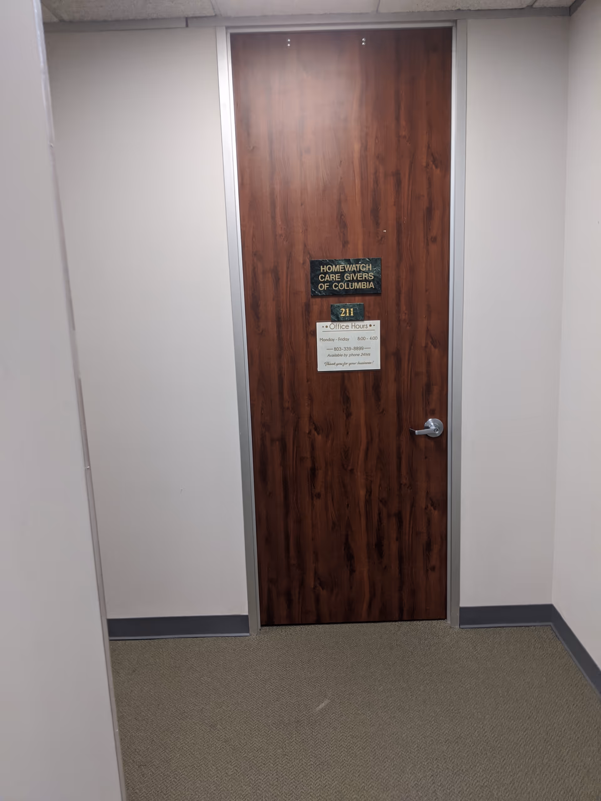 Interior hallway with a wooden door labeled Homewatch CareGivers of Columbia, room 211.