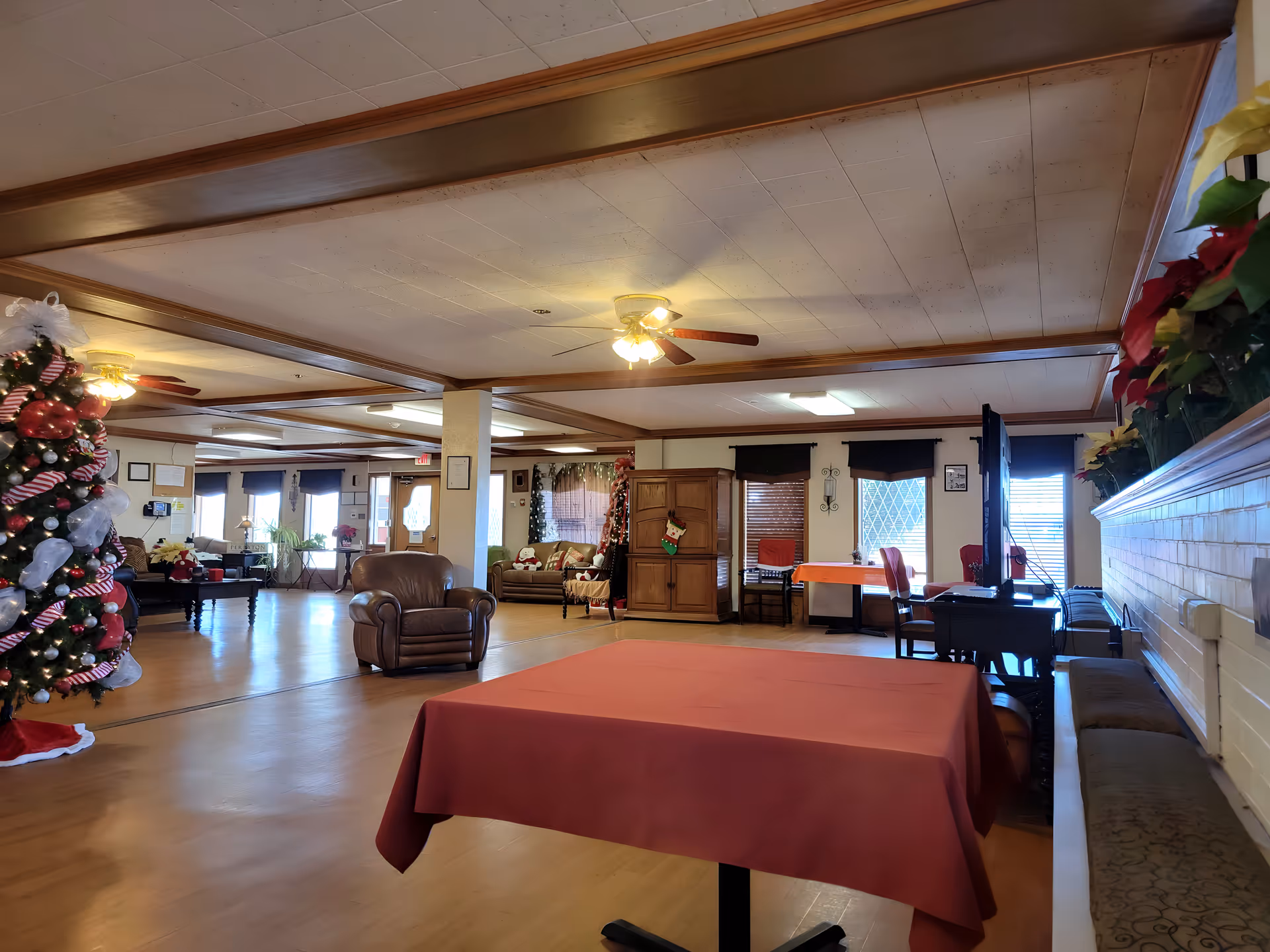 Open senior living facility lounge with Christmas tree, red-draped tables, and seating.