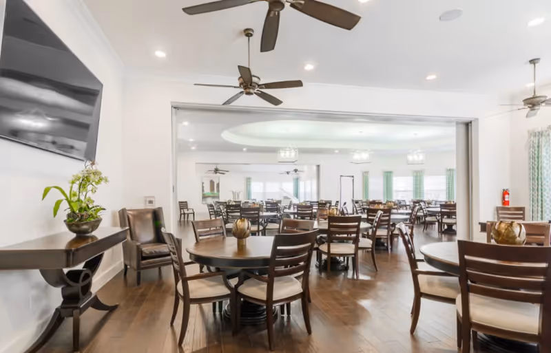 Bright dining hall at Winslow Commons with round tables, chairs, ceiling fans, and an open entry.
