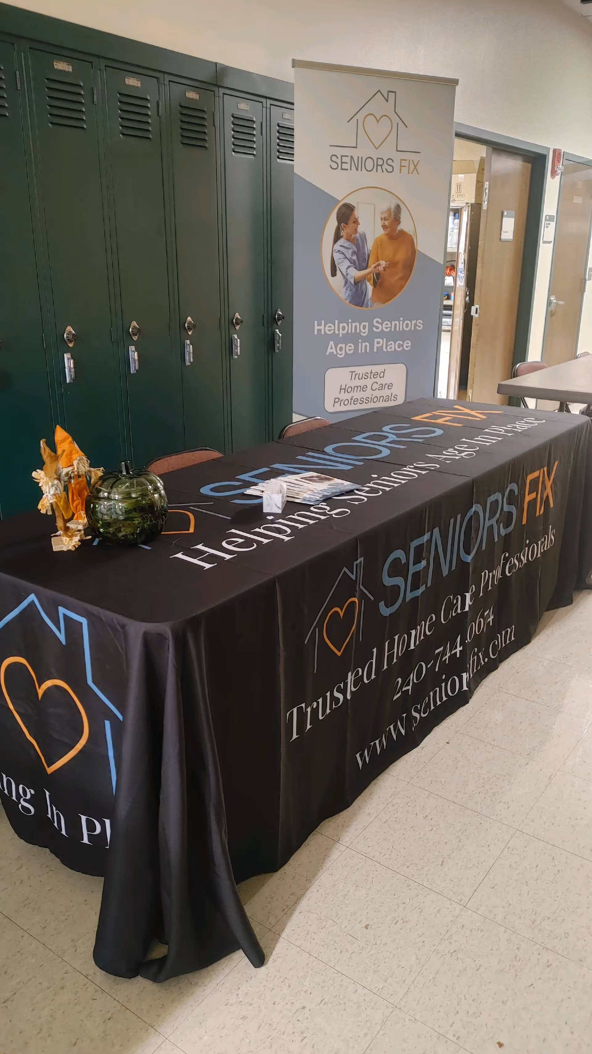 Promotional table with banner for Seniors Fix in a hallway with green lockers.