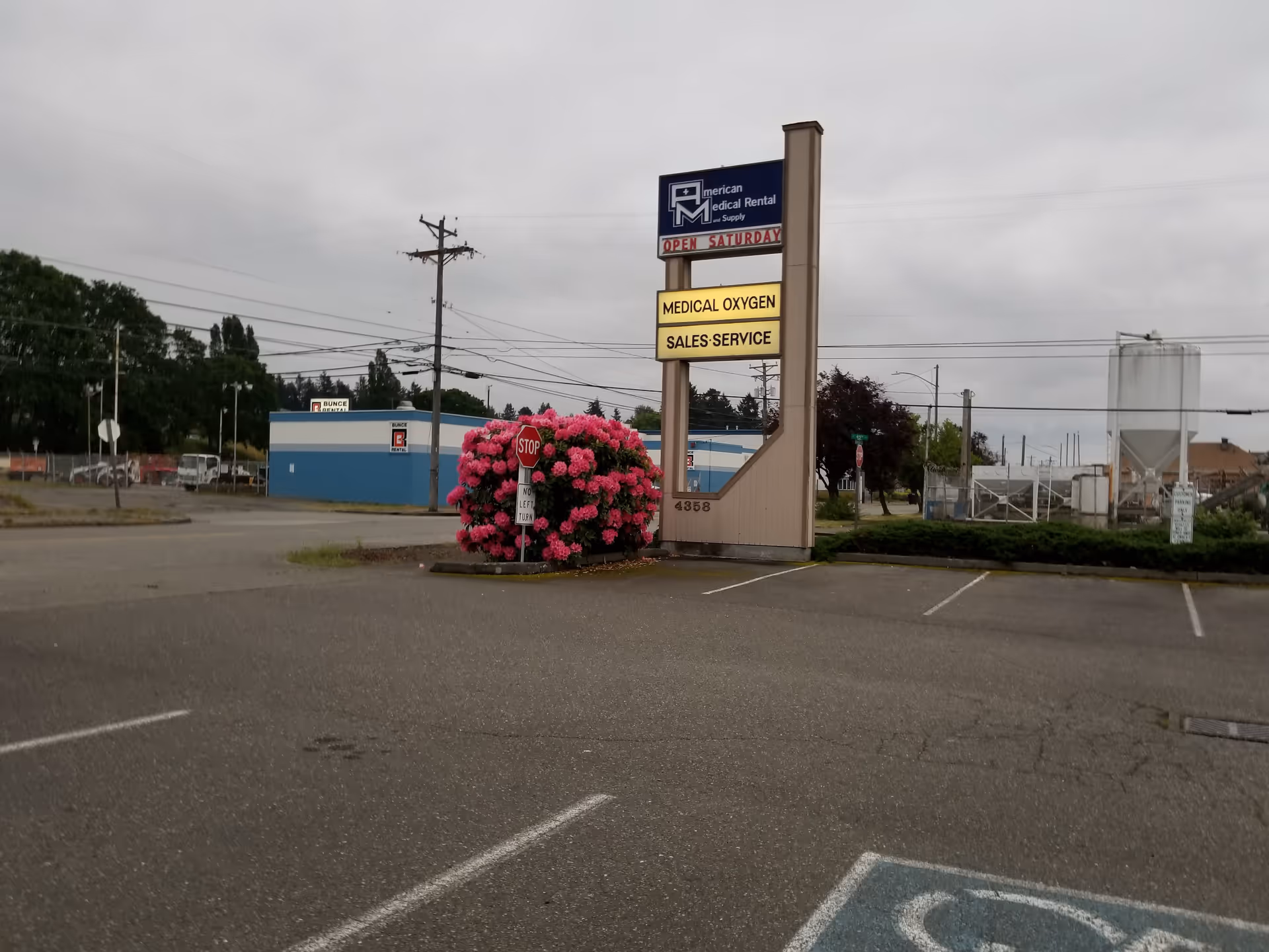 Tall sign for American Medical Rental and Supply beside parking lot and pink flowering bush.