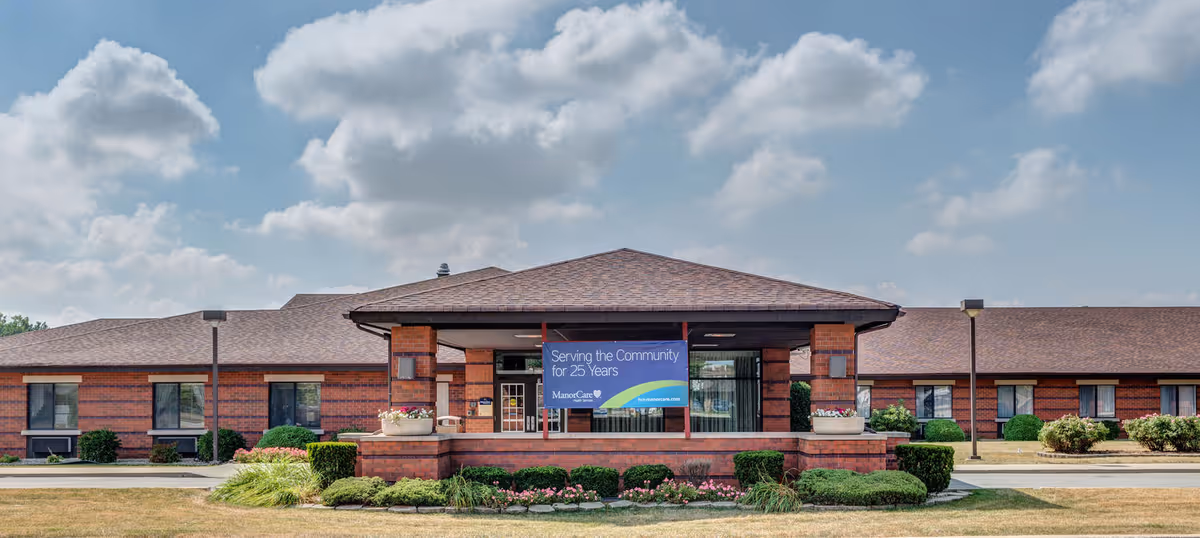 Brick senior living facility with a covered entrance, banner, and manicured landscaping.