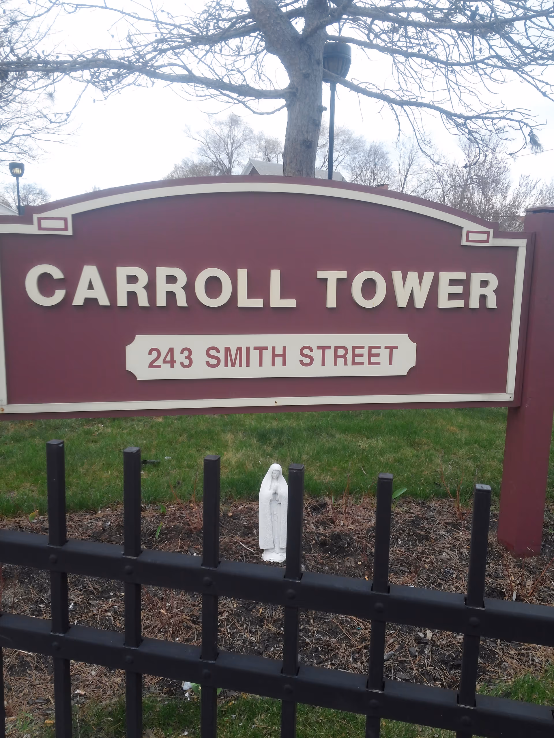 Maroon Carroll Tower sign with address 243 Smith Street, a small statue, and black fence.
