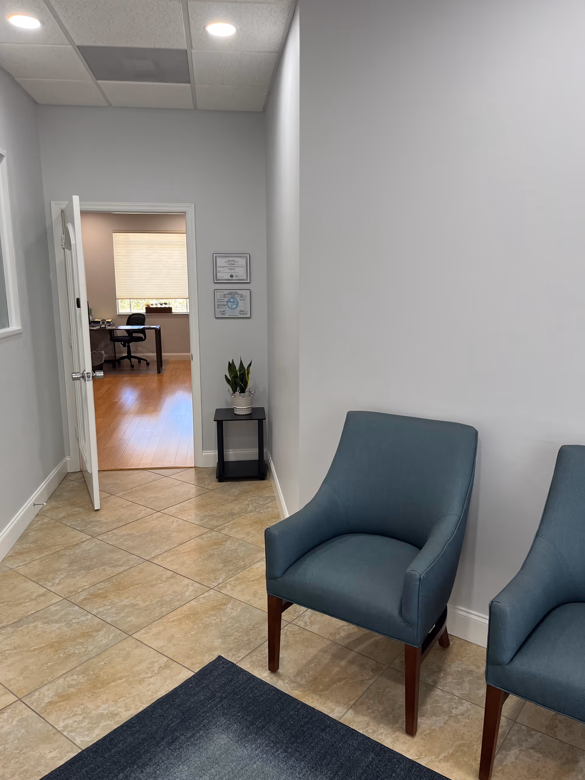 Hallway waiting area at Collier Home Care with blue chairs and an office seen through doorway.