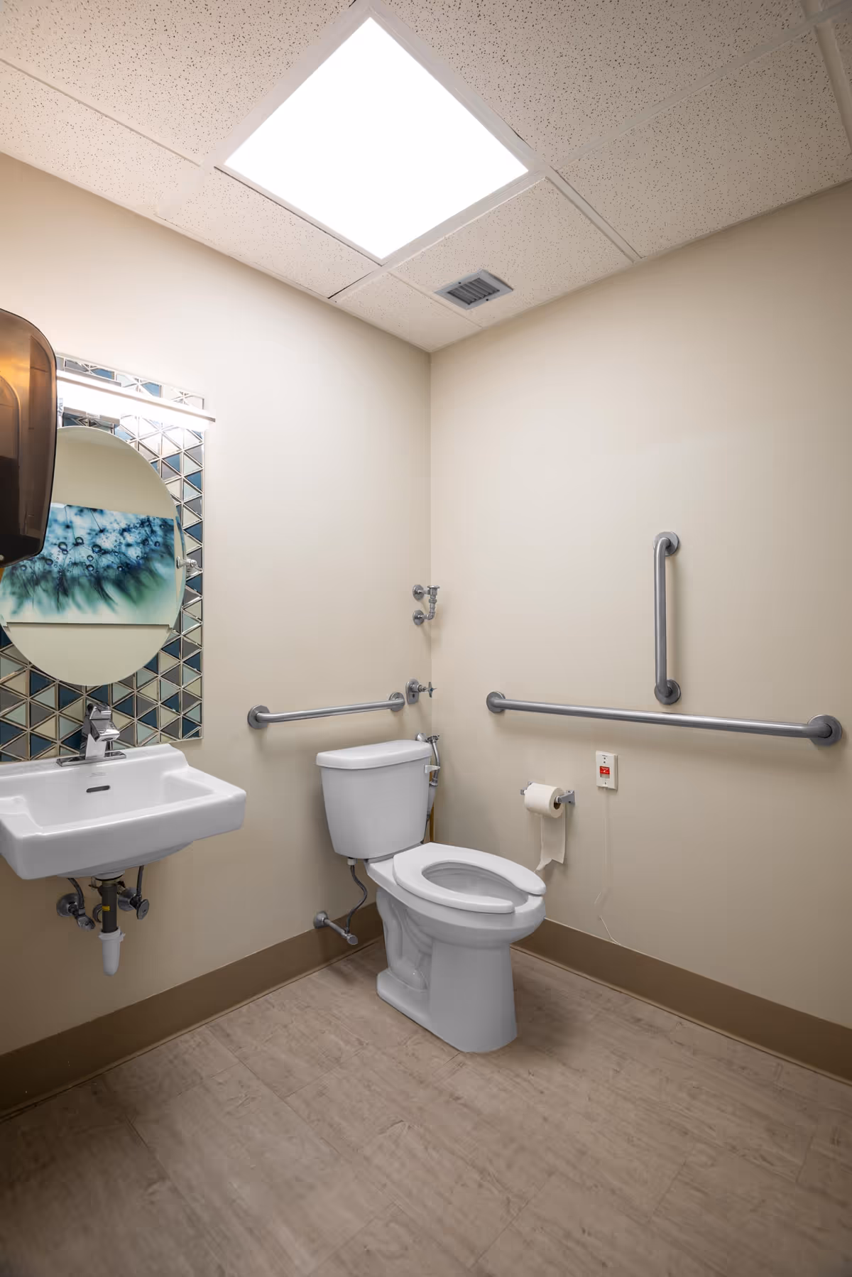 Accessible bathroom with sink, toilet, mirror, and multiple grab bars in a beige room