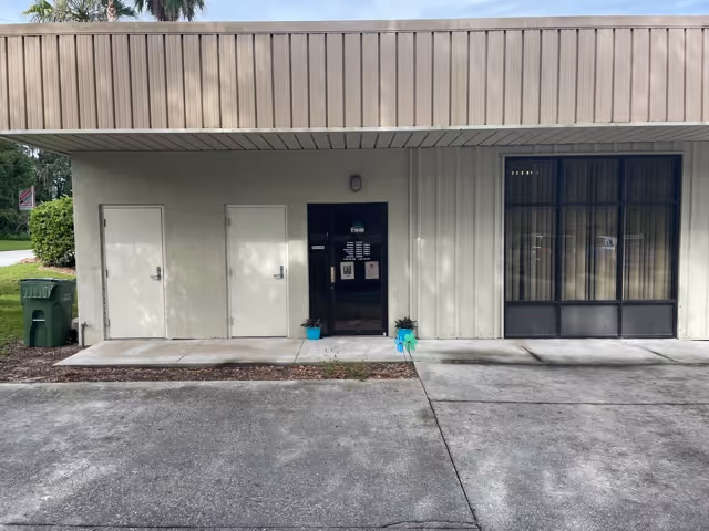 Front entrance of a single-story facility with white doors and a large window.