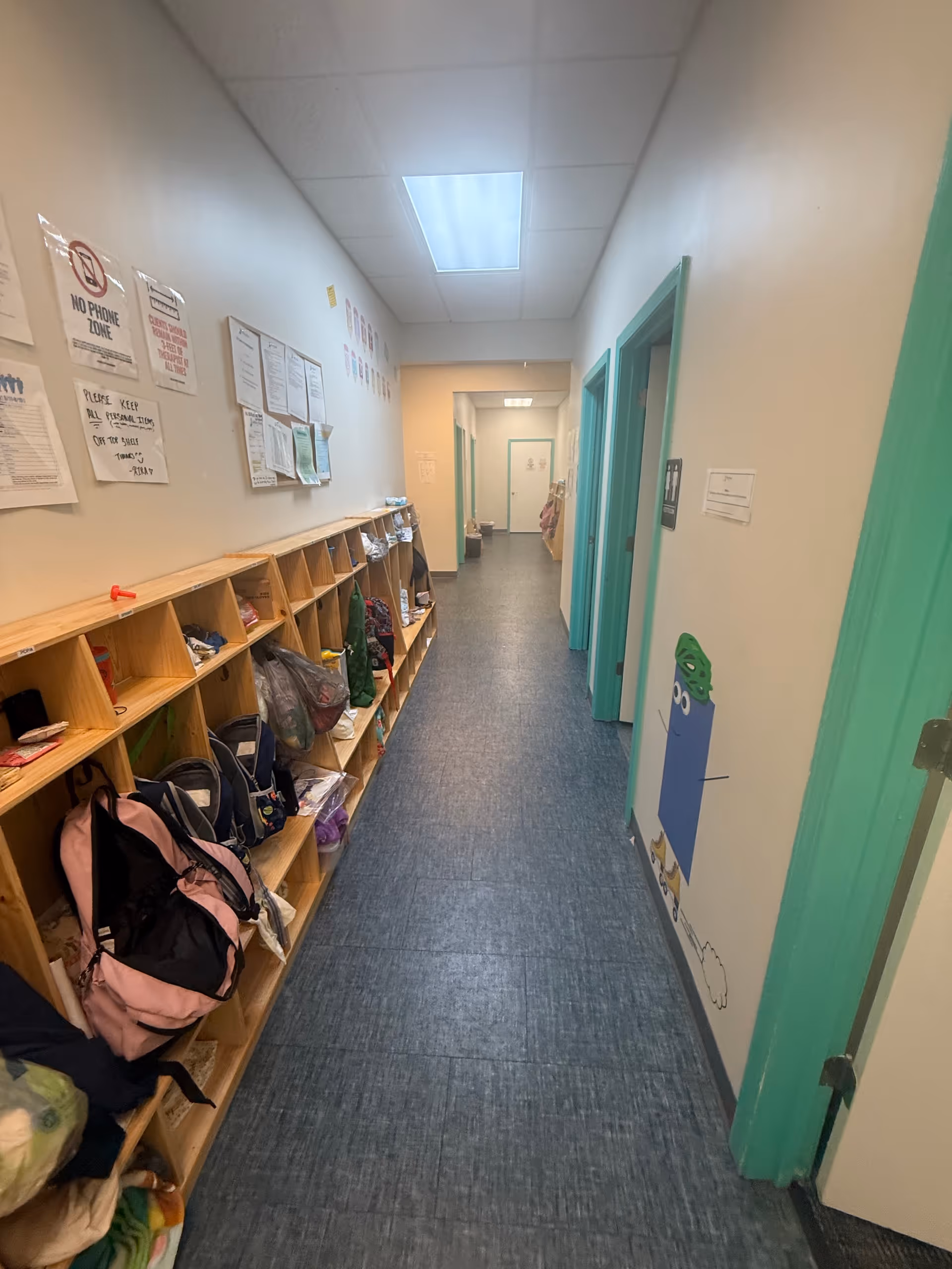 Long hallway with cubbies and backpacks along the left wall.