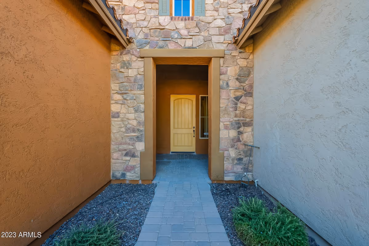 Stone-walled building entrance with a yellow door, archway, and gravel landscaping.