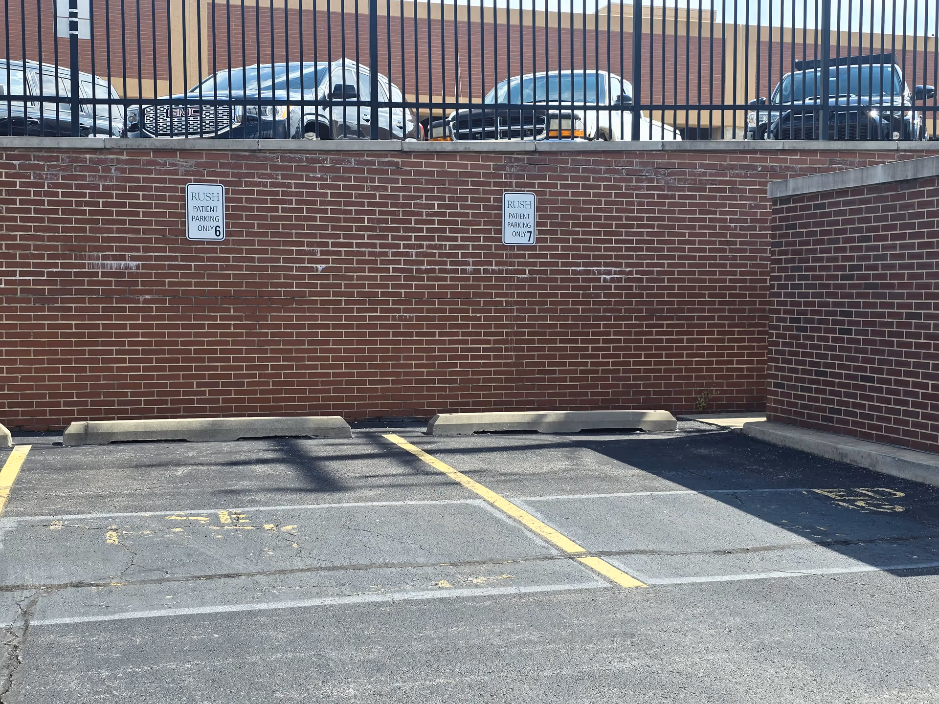 Exterior brick wall with parked cars above and Rush patient parking signs.
