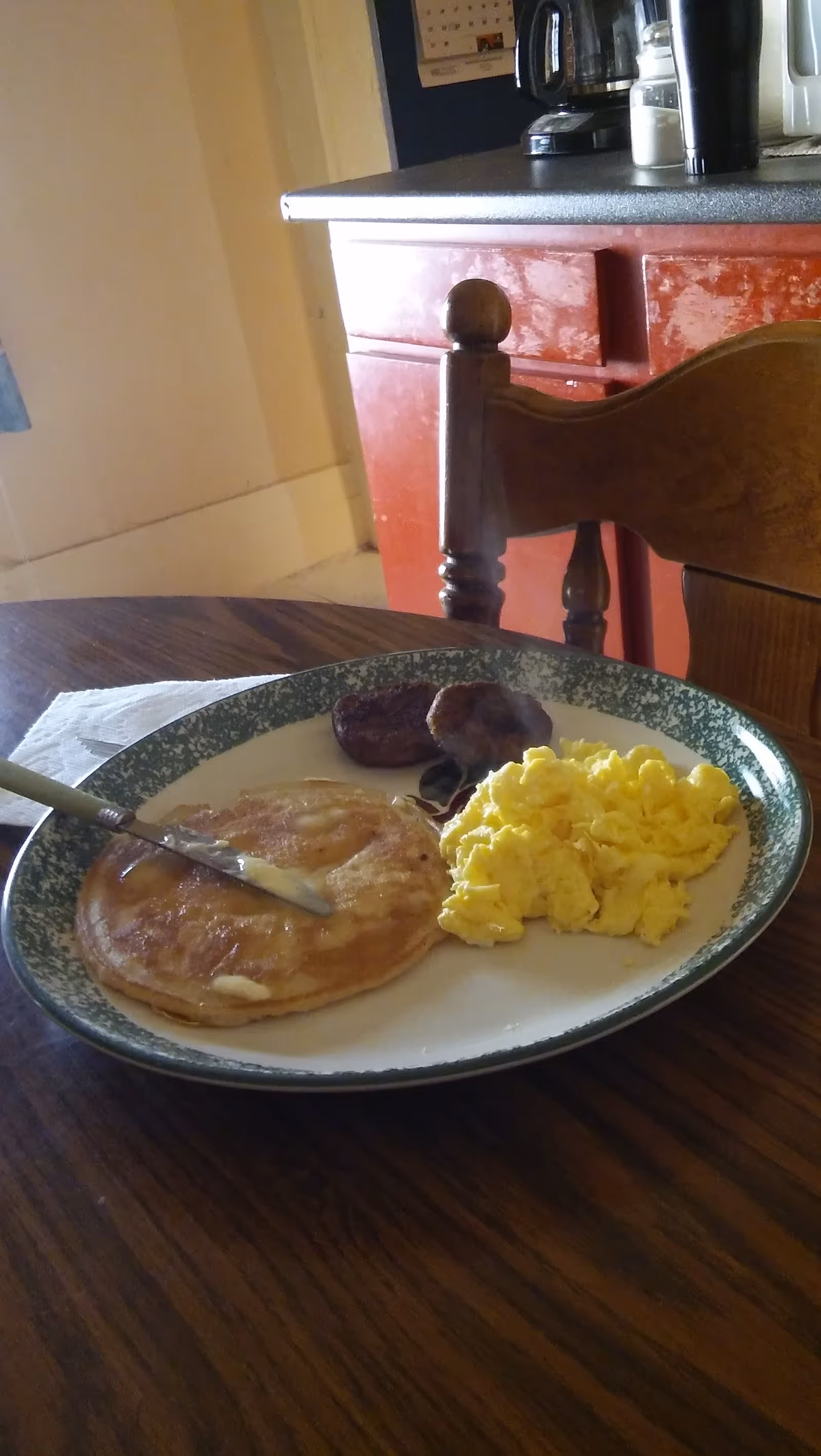Plate of pancakes, eggs, and sausage on a dining table.