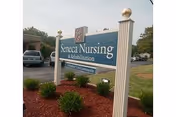 Exterior view of a Seneca Nursing & Rehabilitation Center sign with landscaped shrubs and parking.