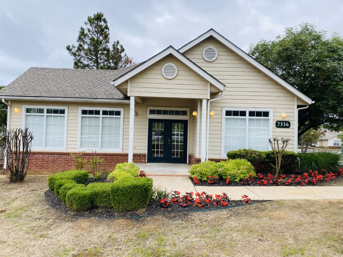Beige single-story senior living building with front entrance and manicured shrubs.