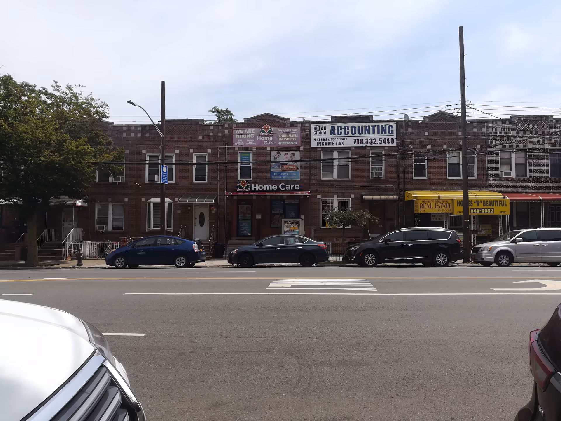 Brick storefront row along a street with parked cars and a Home Care sign.