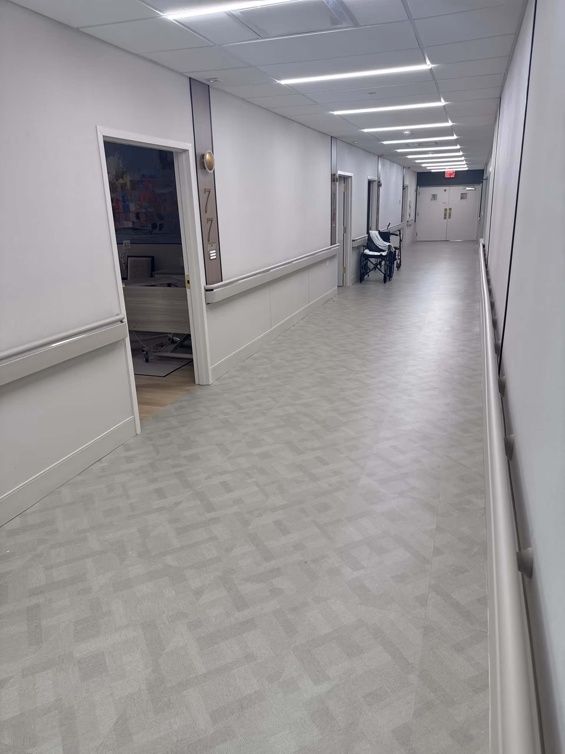 Long interior hallway in a senior living facility with doors and a wheelchair.