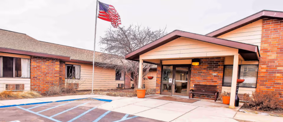Senior living facility front entrance with American flag, brick exterior, bench, and handicap parking.