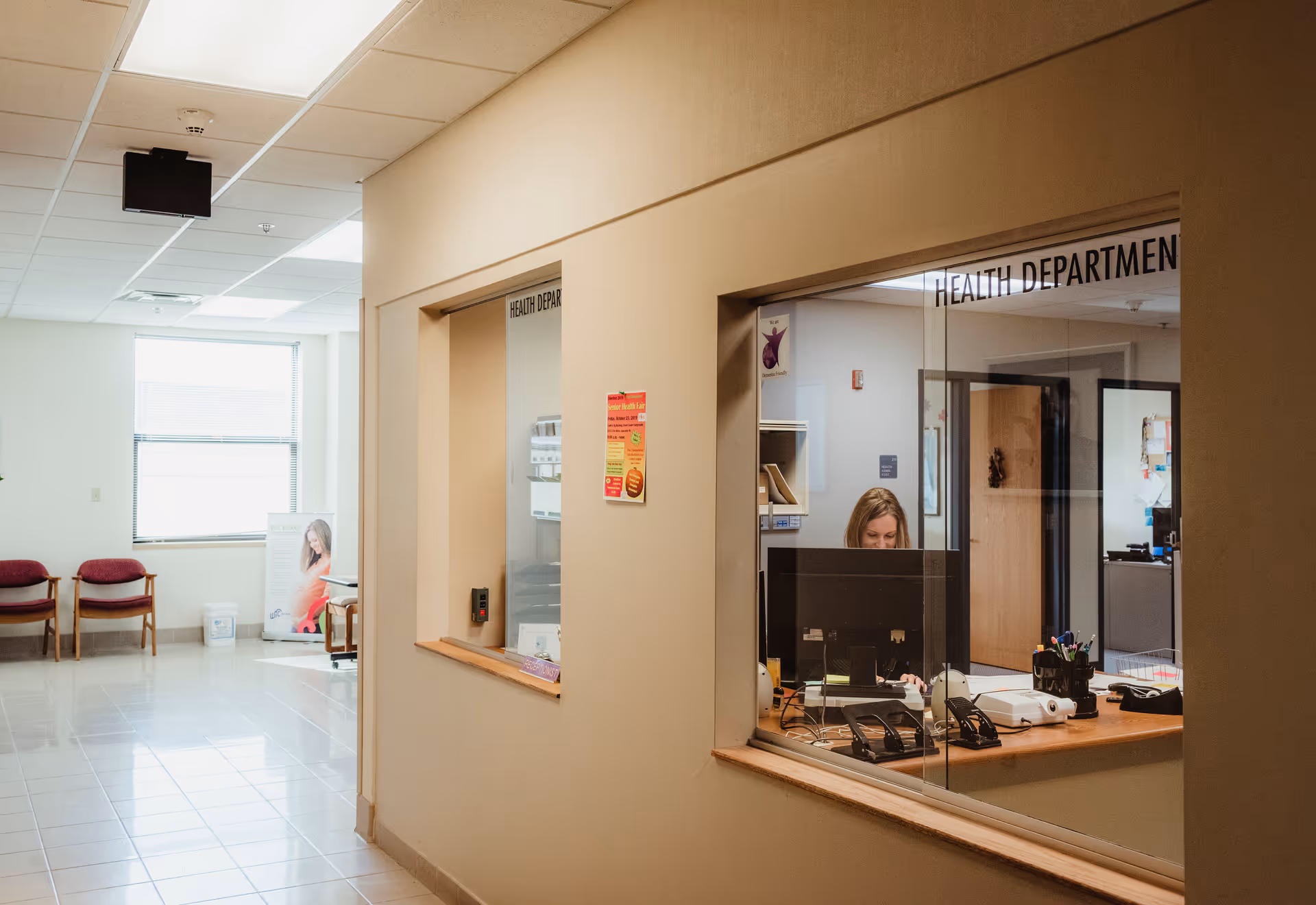 Interior of a health department reception area featuring a front desk window and seating