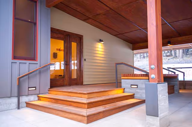 Wooden steps lead to a covered porch and glass entrance of a modern adult family home.