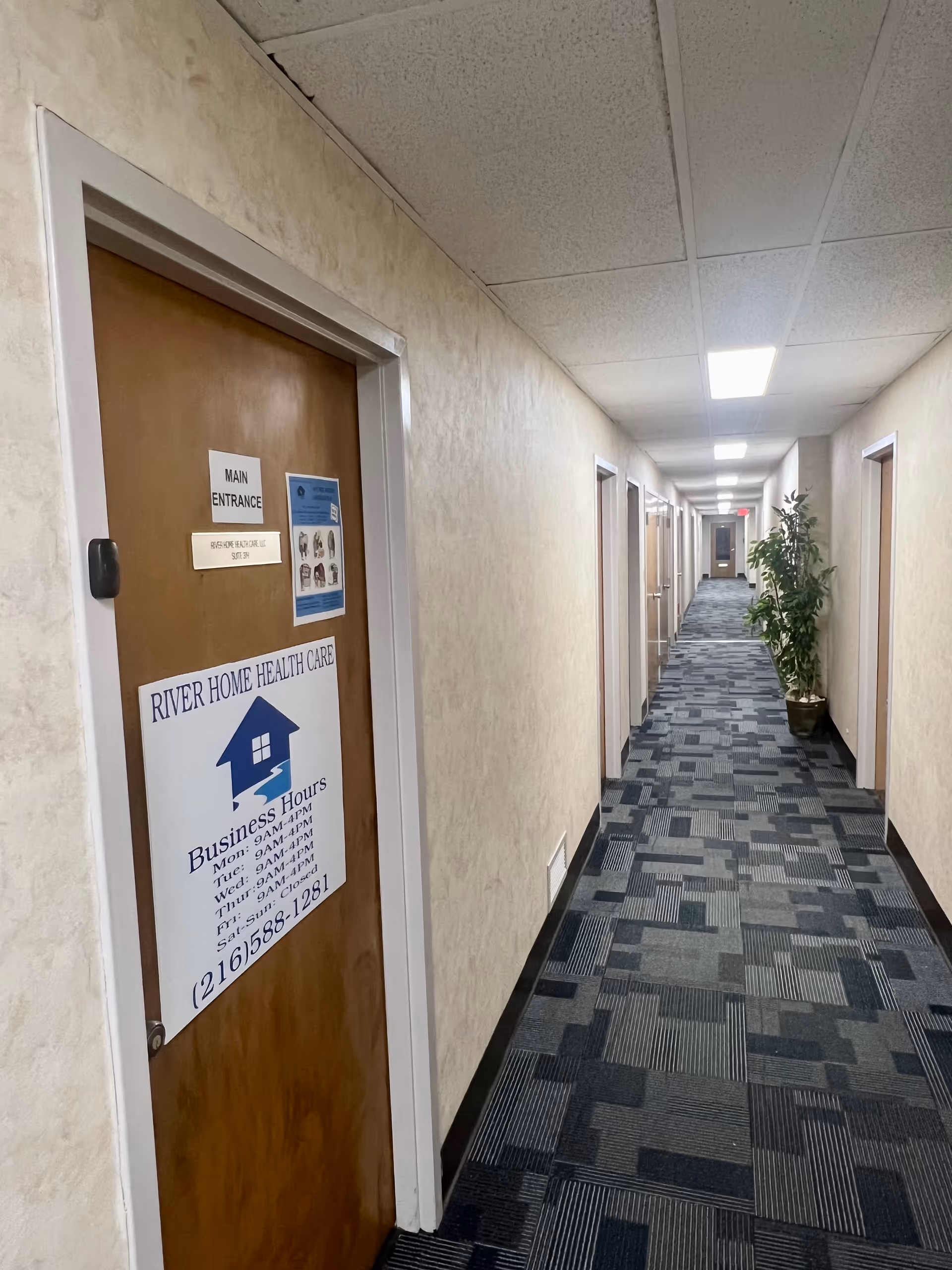Long hallway inside River Home Health Care facility with doors, carpet, and a potted plant.