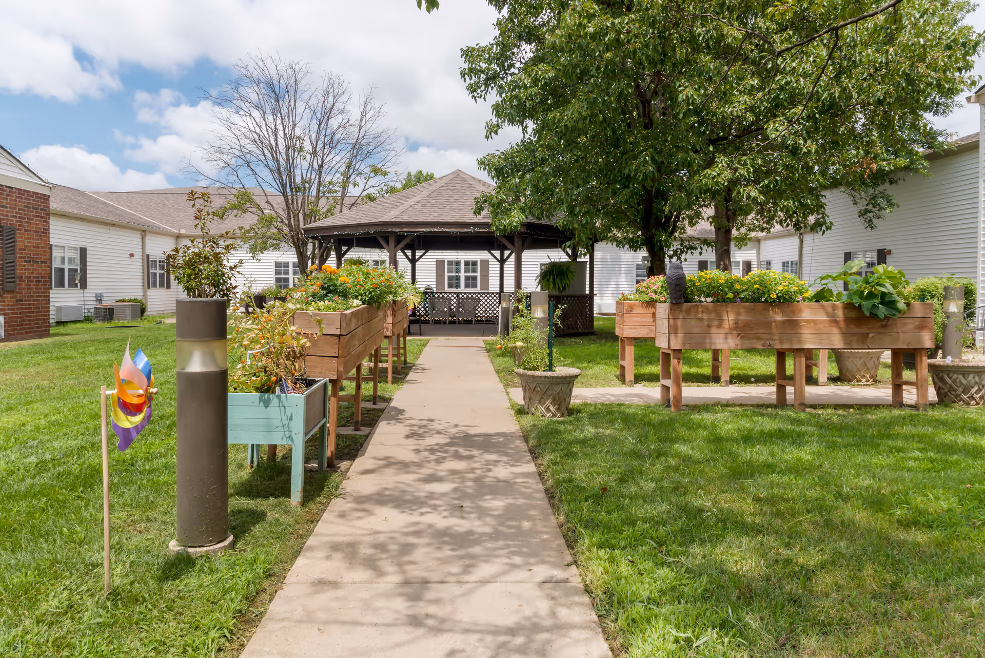 Path through a grassy courtyard with raised planters and a gazebo at Stratford Commons Memory Care