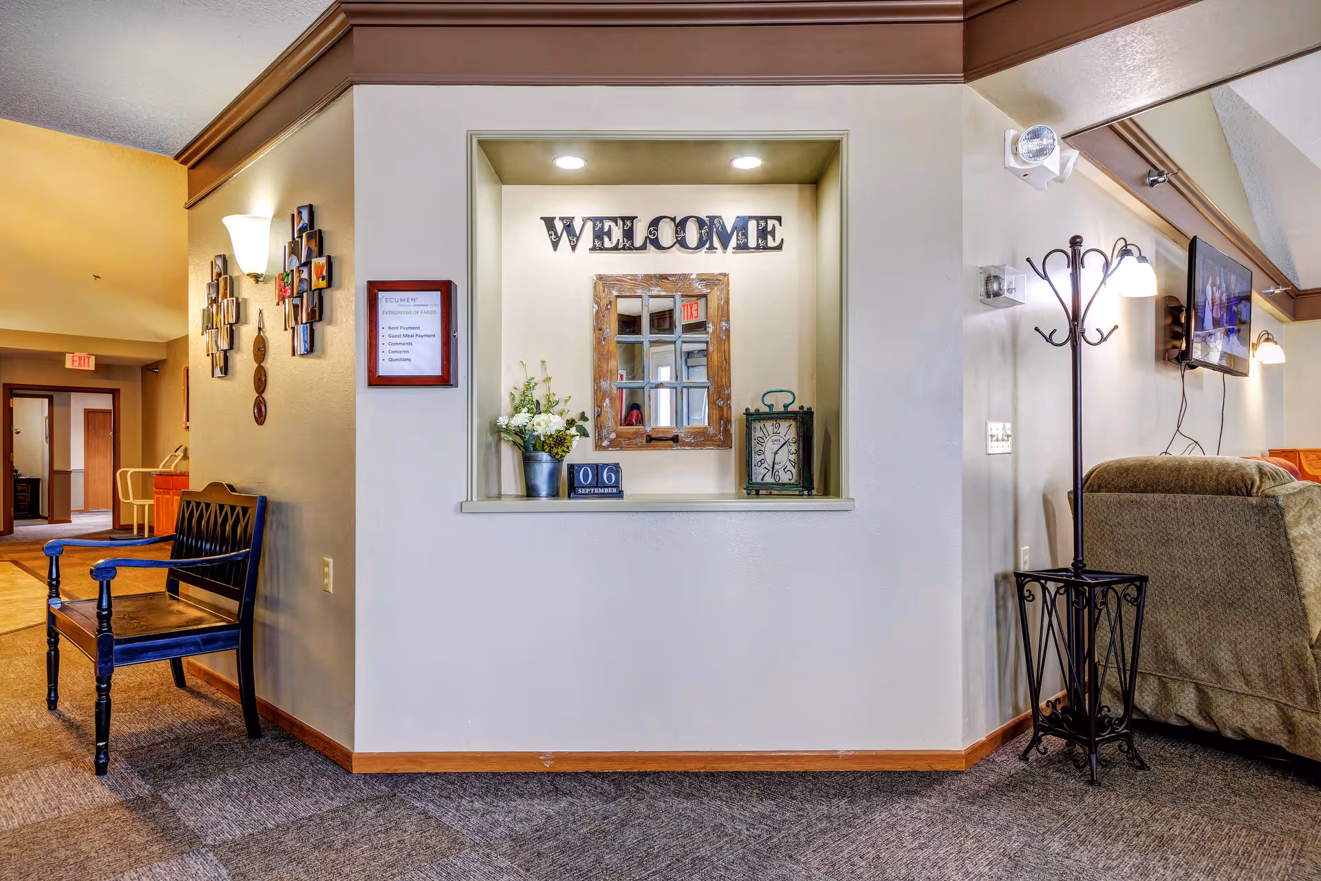 Indoor lobby featuring a welcome window, plant, clock, seating, and wall-mounted TV.