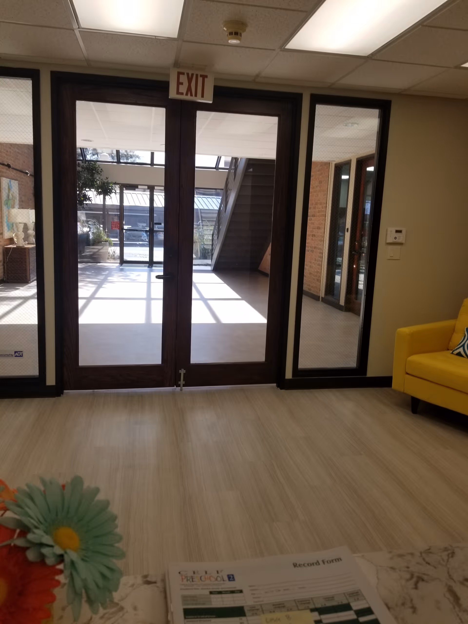 Interior lobby area with glass doors, exit sign, and yellow seating.