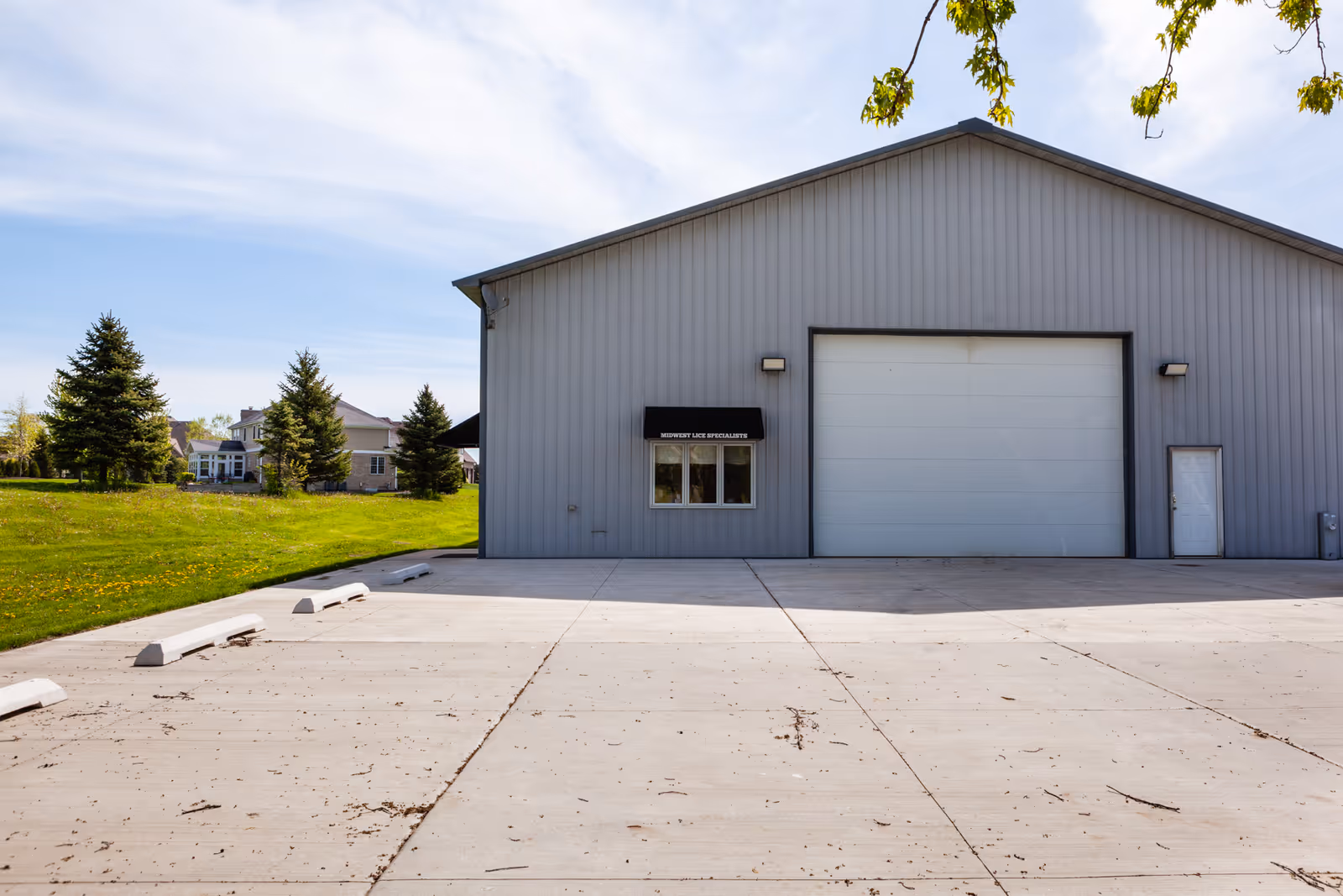 Large gray metal building with a tall garage door and small window beside a green lawn.