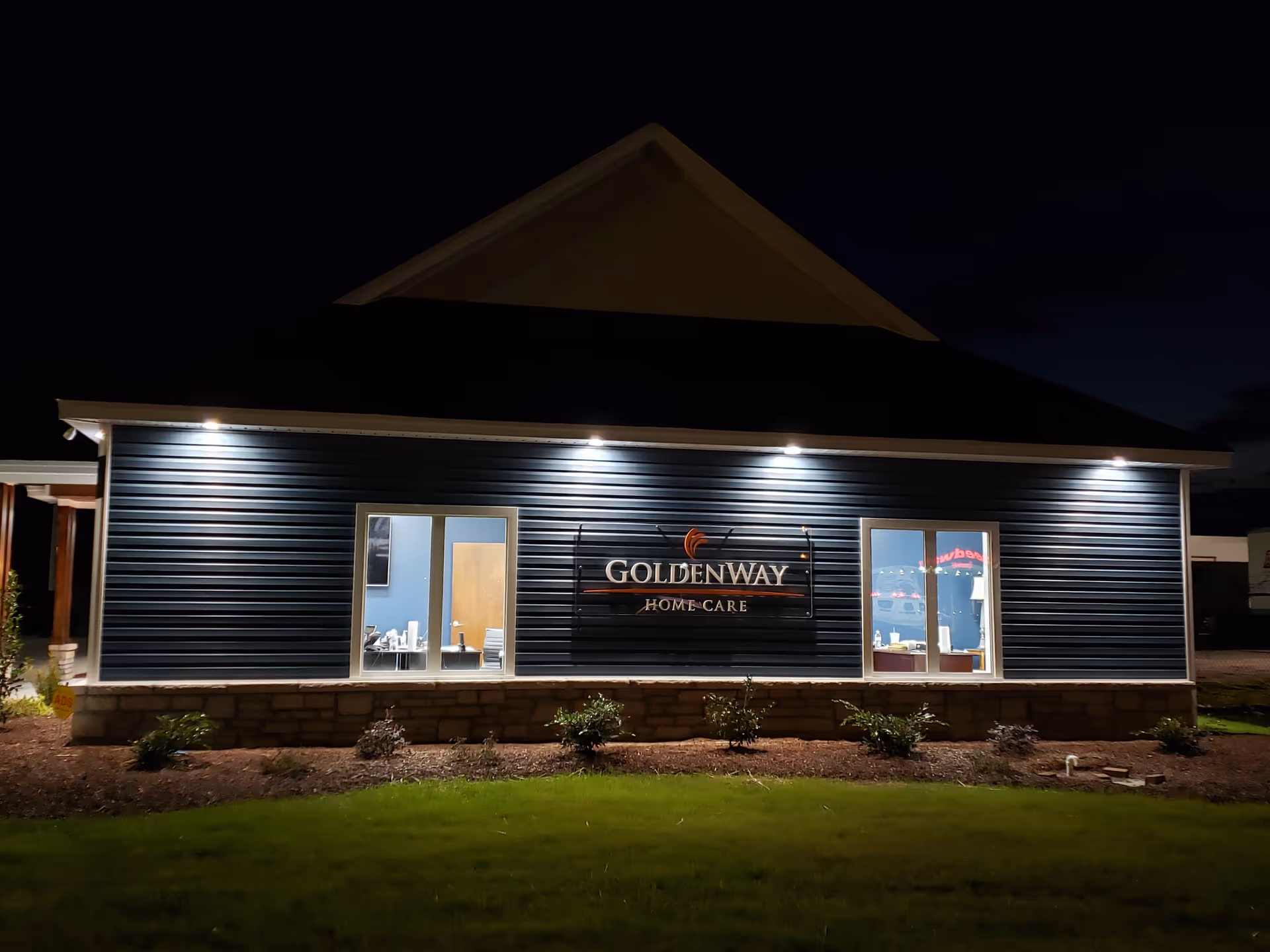 Night exterior of a single-story building with a lit sign reading Golden Way Home Care.