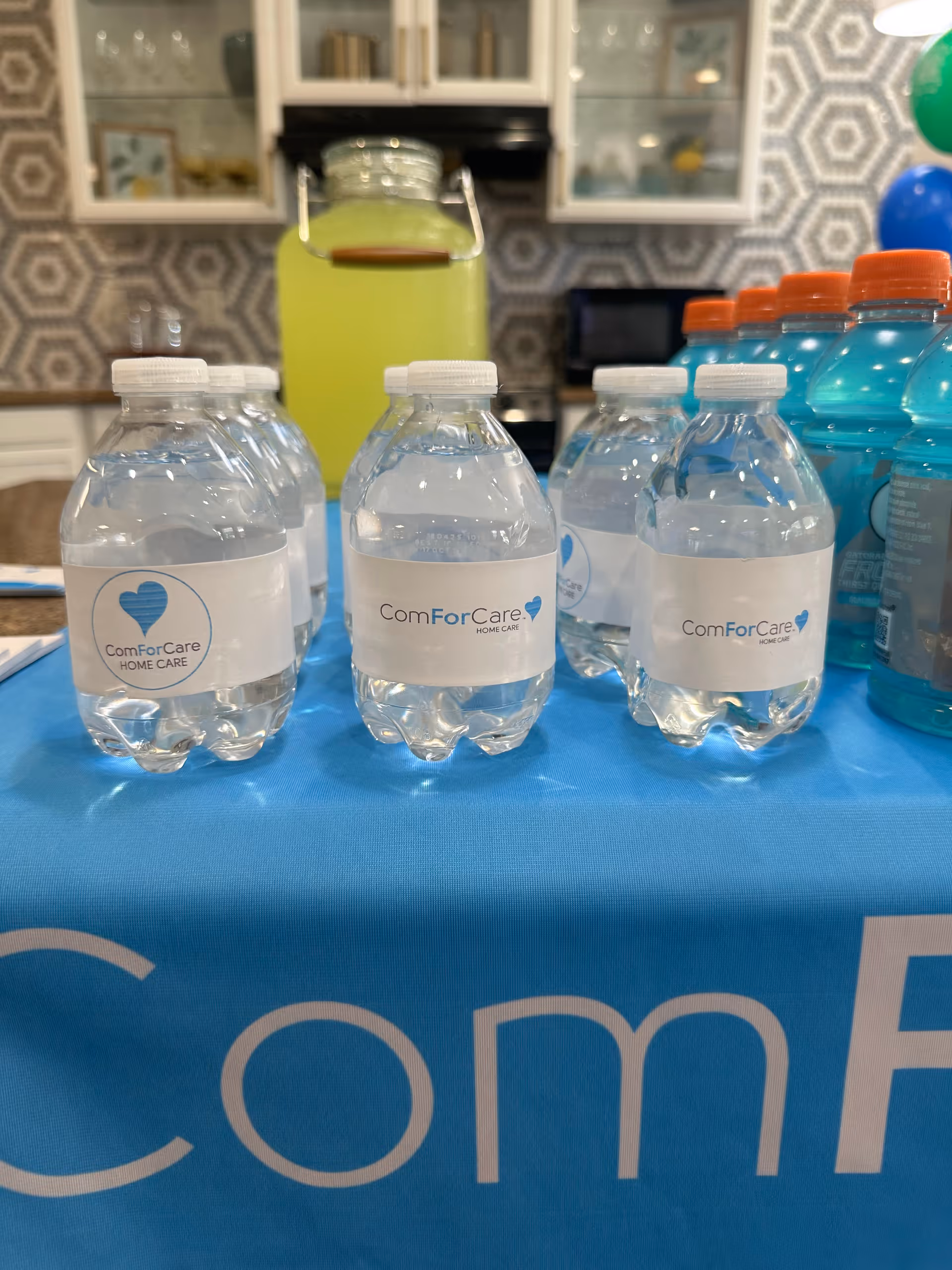 Water bottles labeled ComForCare on a blue tablecloth inside a facility kitchen area.