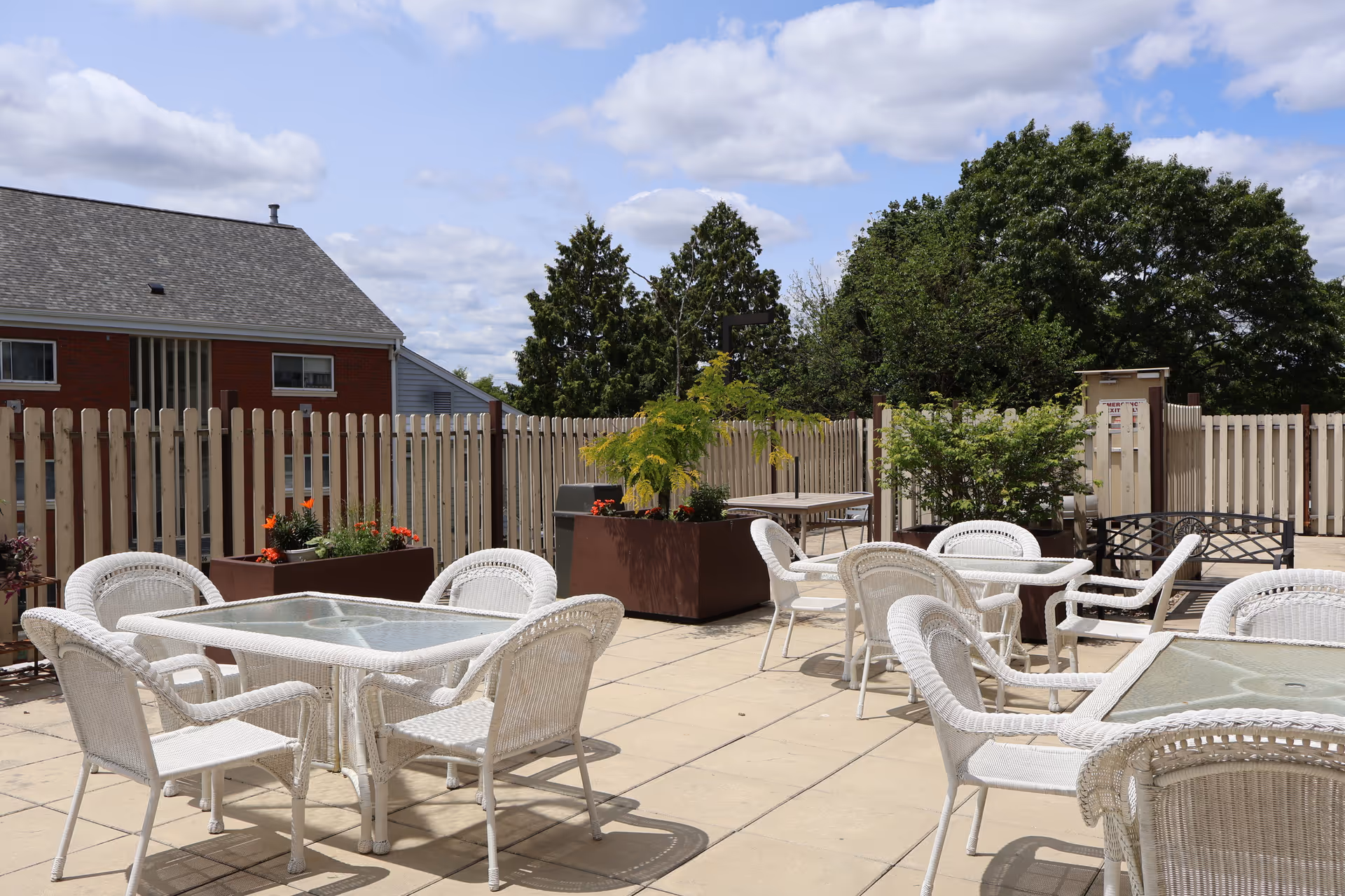 Outdoor Bannister Center patio with white wicker tables and chairs, planters, and a wooden fence.