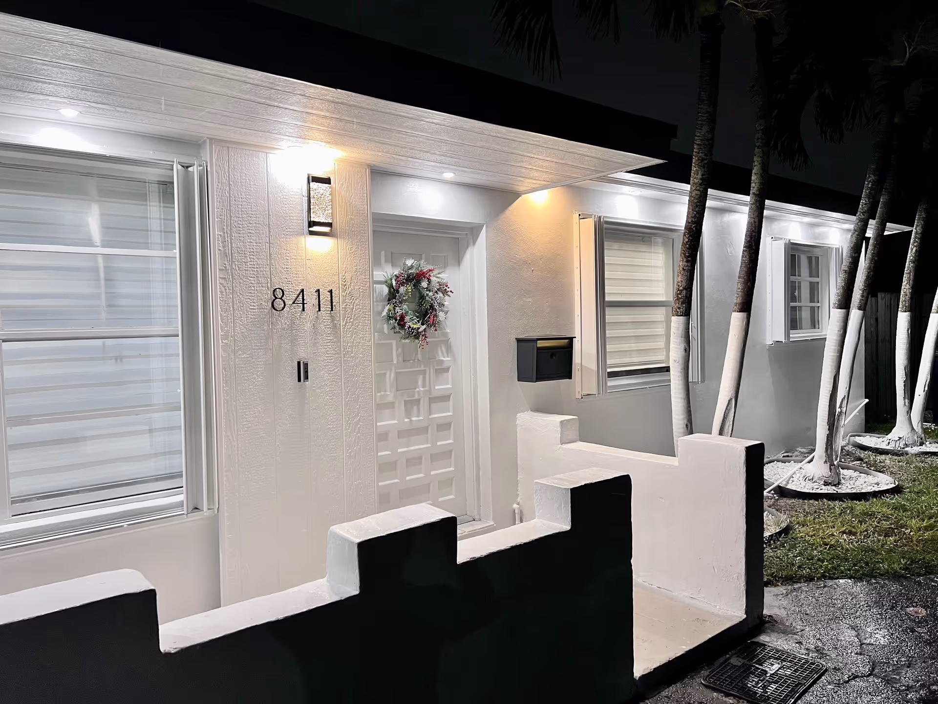Night exterior view of a white senior living building entrance at 8411 with a wreath.