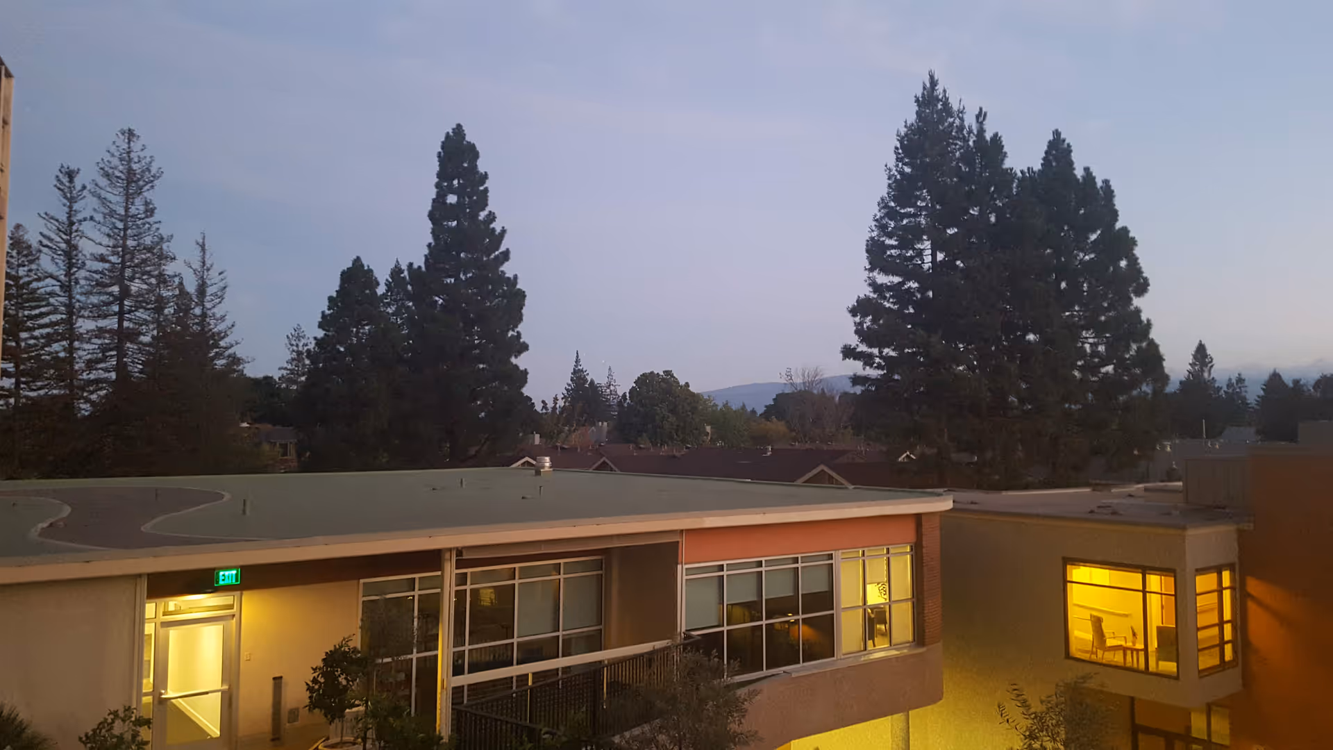 Exterior view of senior living facility with lit windows and palm trees in background at dusk.