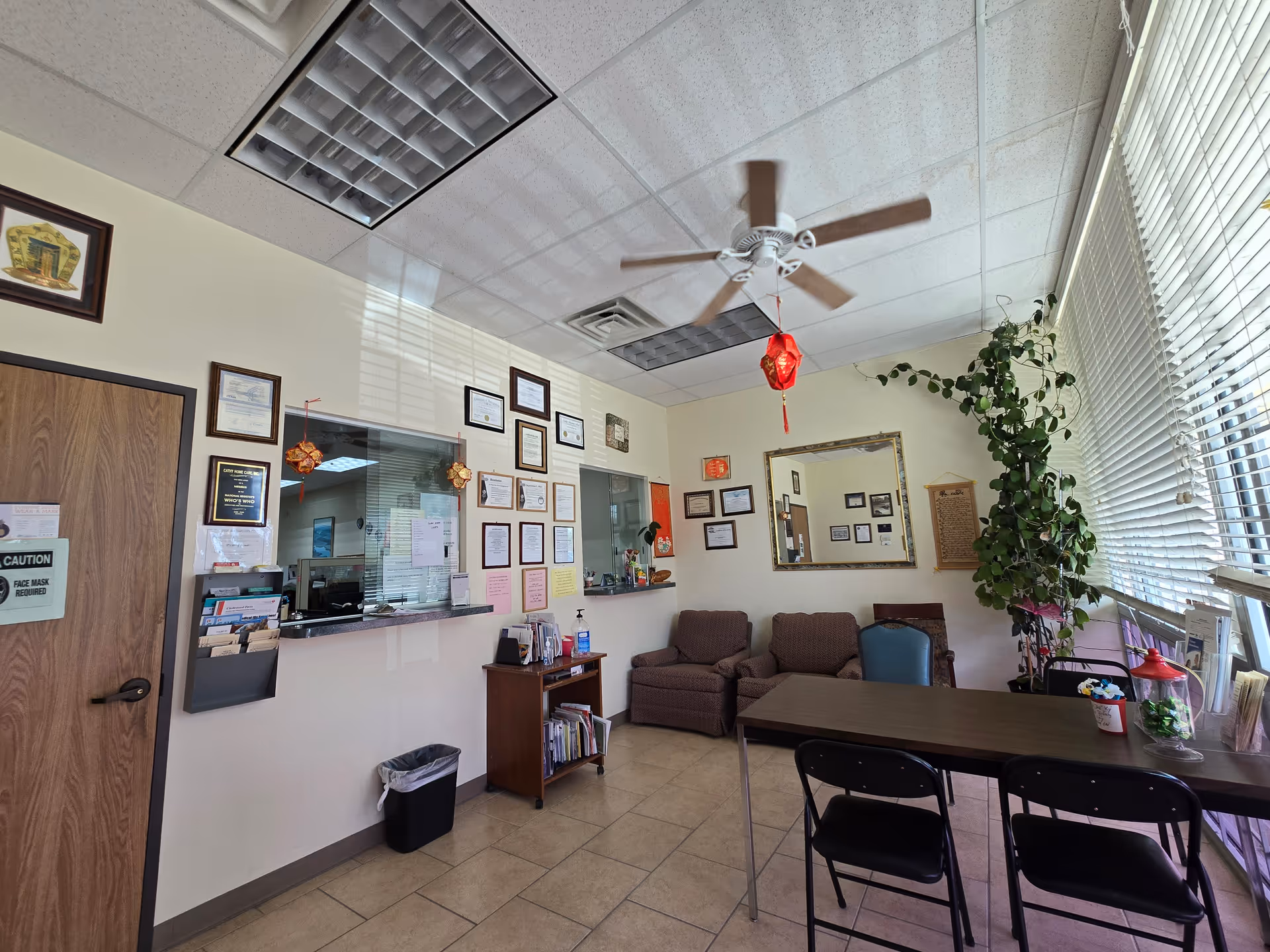 Reception area in a senior living facility with chairs, table, plants, and wall certificates.