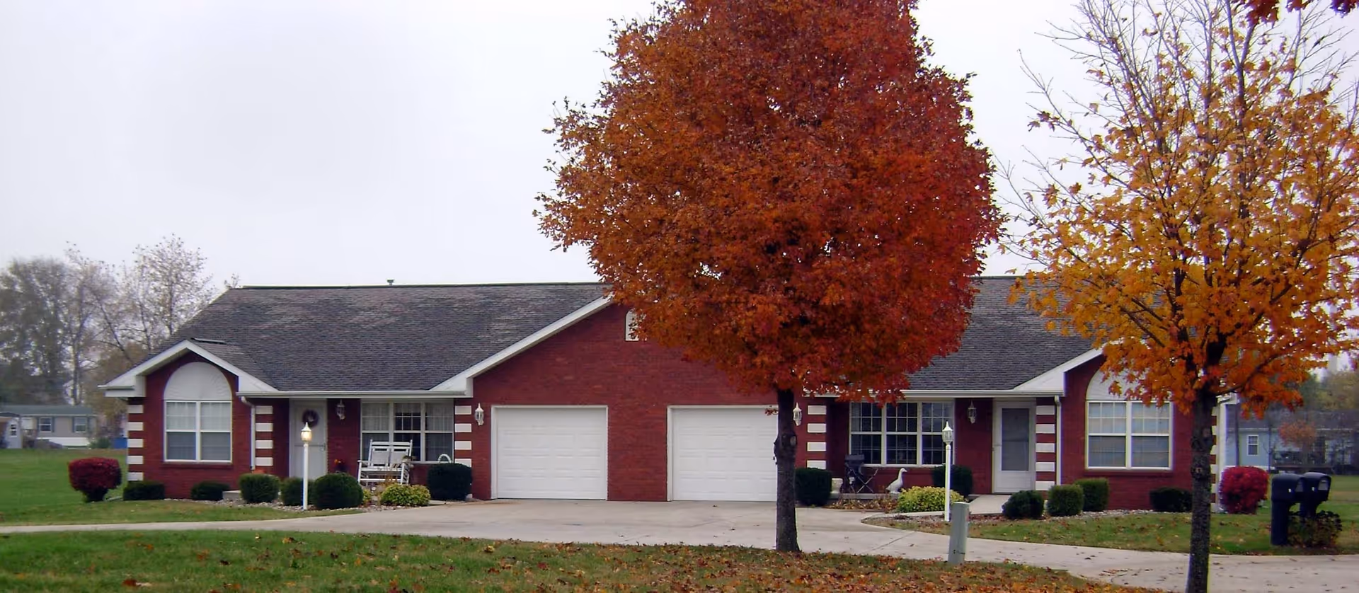 Leroy Manor exterior: a single-story red brick senior living facility with two garages and trees.