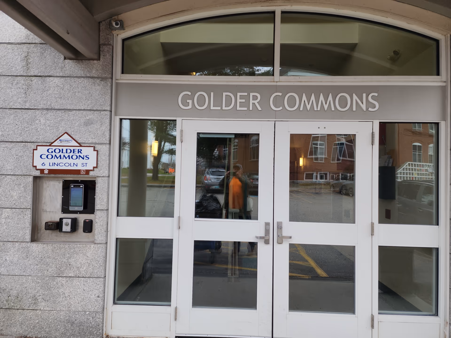 Stone-faced building entrance with glass doors reading GOLDER COMMONS and a street sign.
