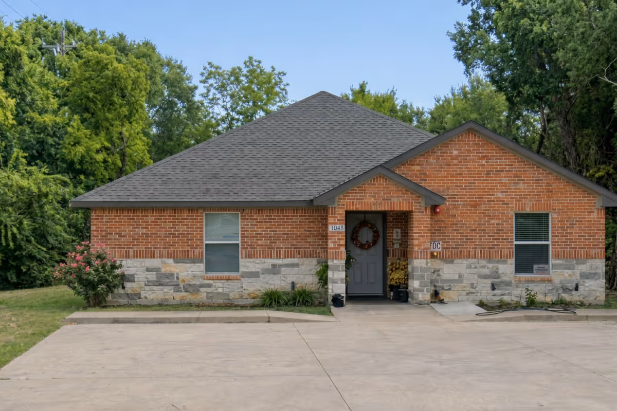 Brick senior living facility with stone base, front entrance, wreath, and surrounding greenery.