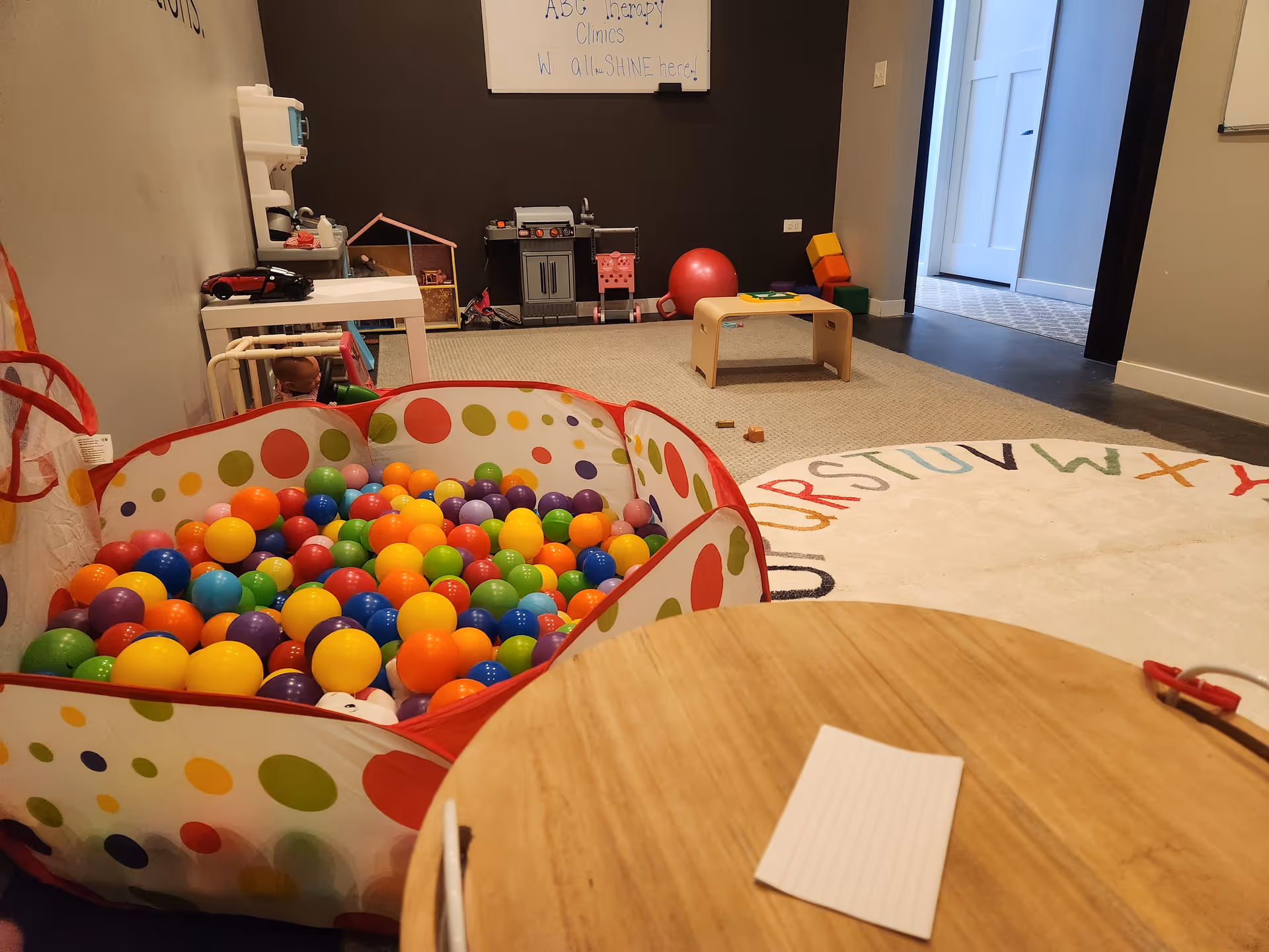 Colorful indoor playroom with a ball pit, toys, and a wooden table.