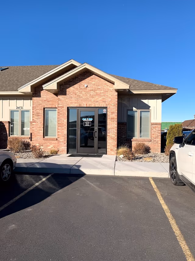 Brick front entrance of a facility with glass doors and a small walkway.
