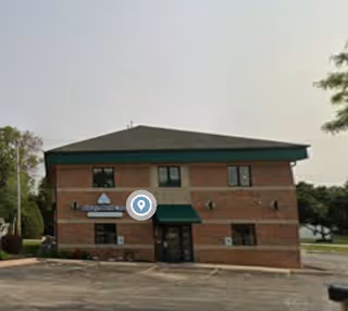 Two-story brick senior living facility with green awnings and a parking lot in front.