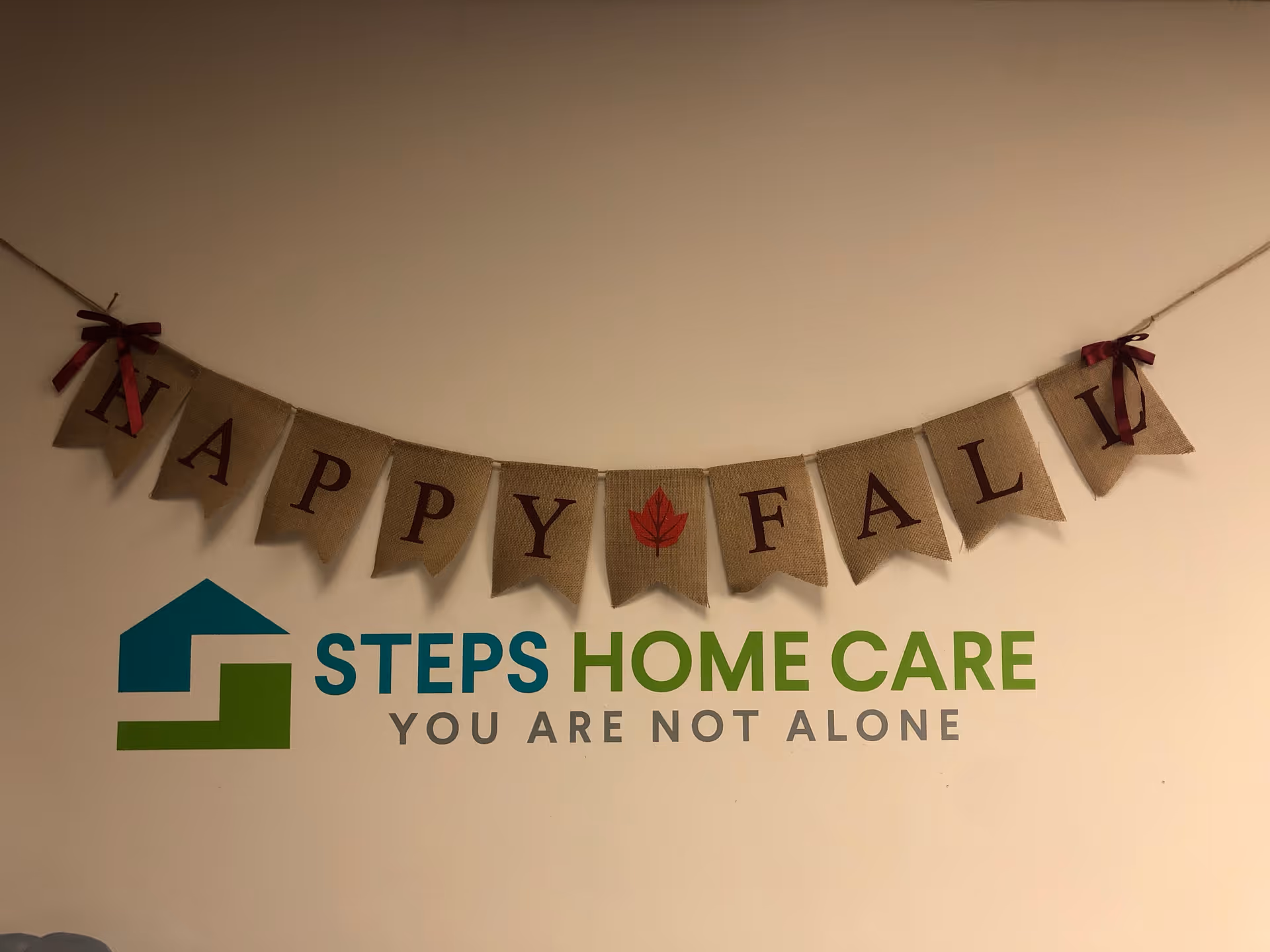 Indoor wall with a burlap banner reading HAPPY FALL above the STEPS HOME CARE logo.