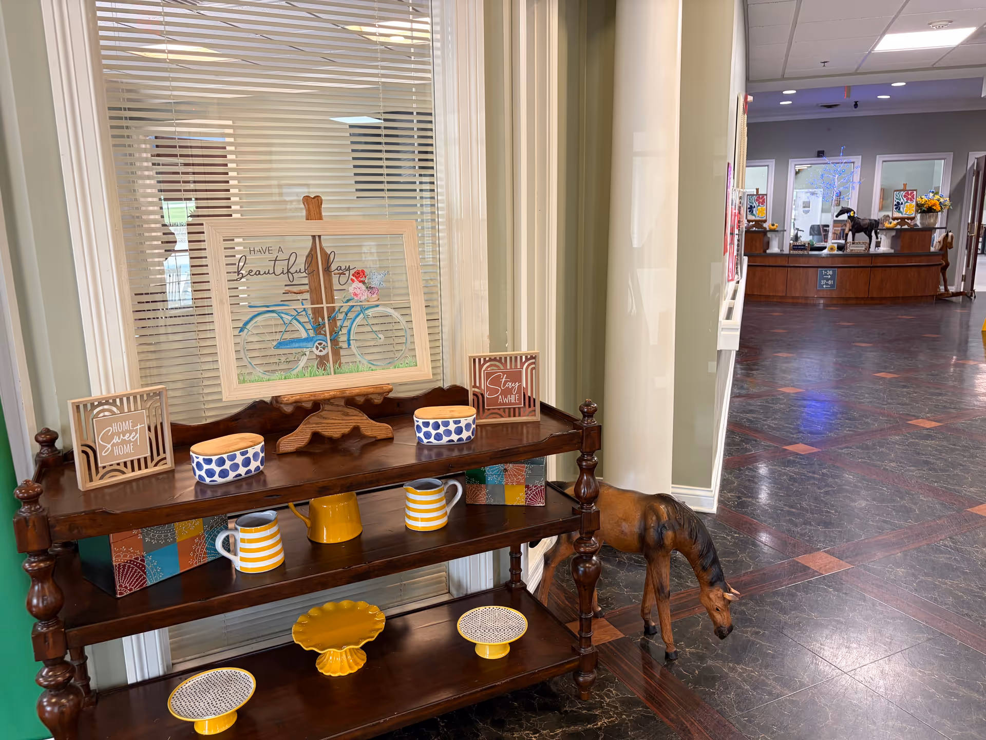 Decorative wooden shelf with mugs, plates, and bicycle artwork in a lobby.