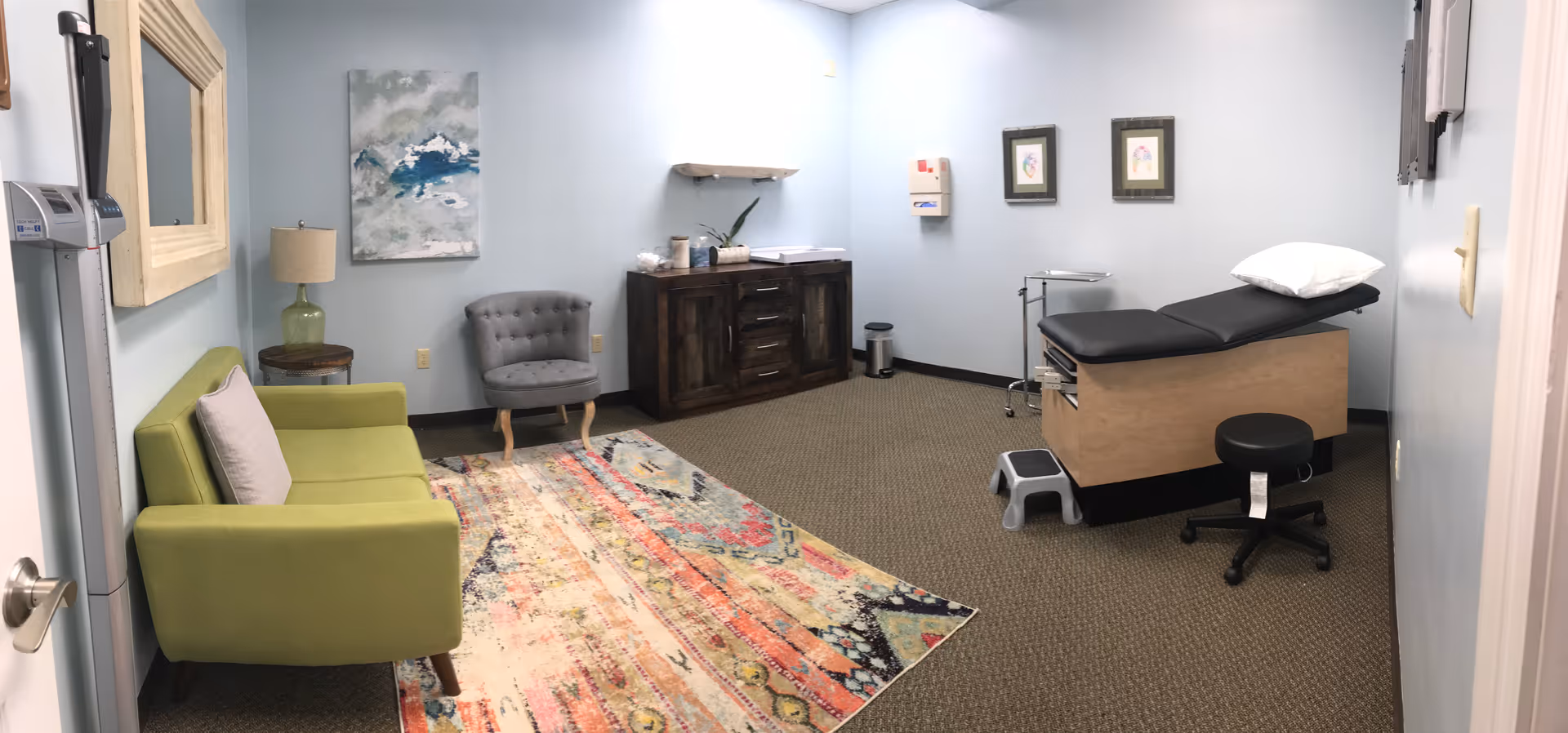 A clinic-style treatment room in a senior living facility with exam bed and seating.