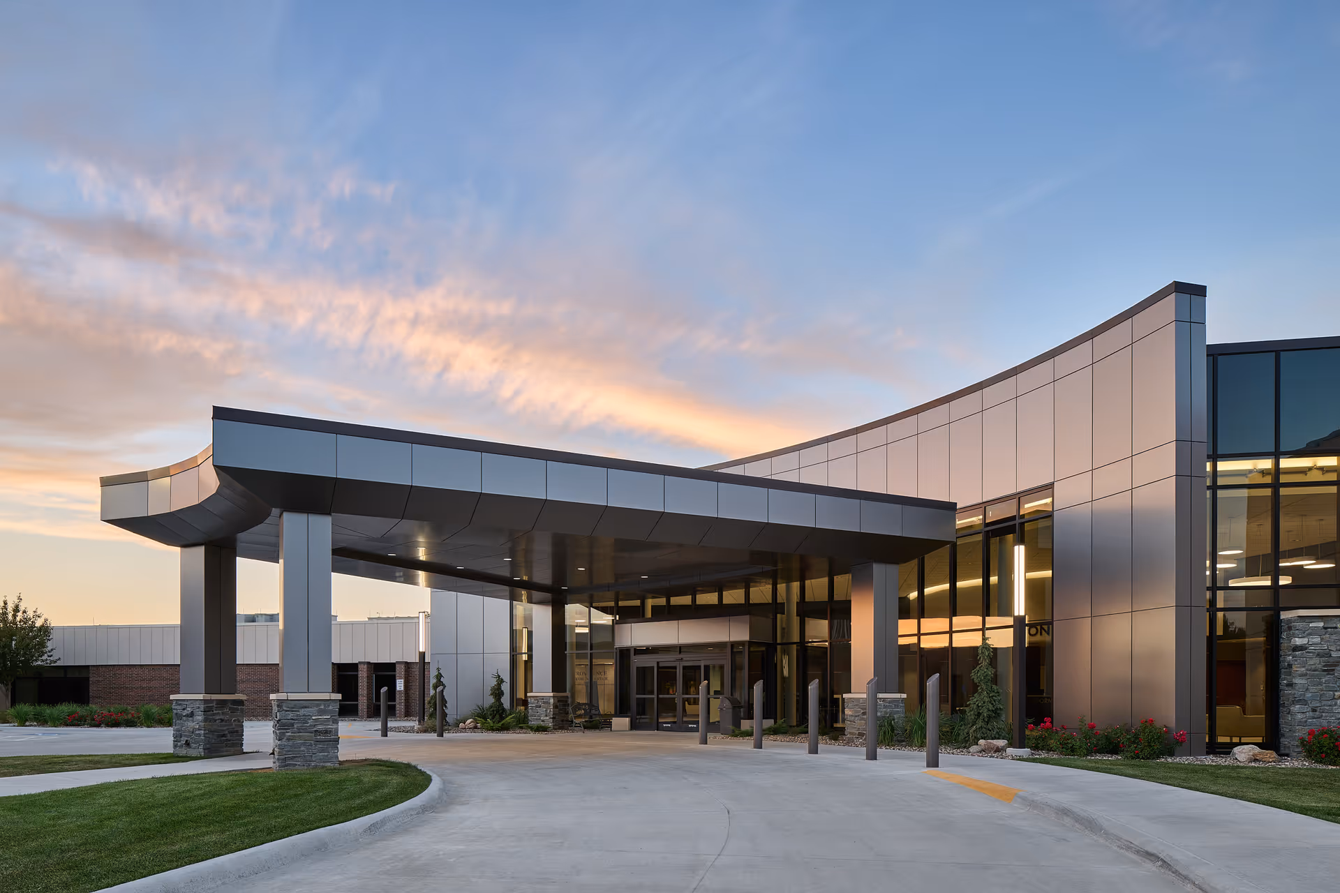 Modern medical facility exterior with glass entrance and curved canopy over driveway at sunset.